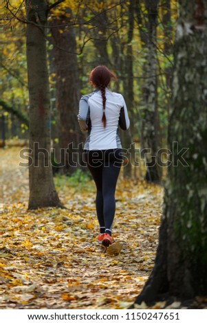 Photo from back of young brunette woman running through autumn park