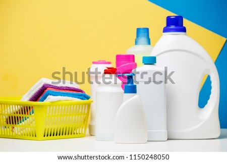 Photo of several bottles of cleaning products and multi-colored towels in basket isolated on blue, yellow background