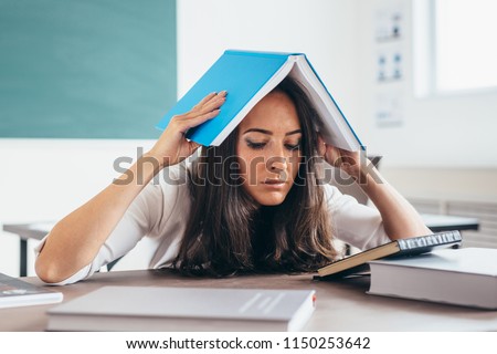 Tired girl studying at working table. Exhausted female student reading books.