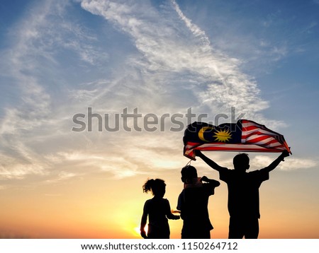 Silhouette of children waving the national flag in conjunction with Malaysia Independence Day. Selective focus.  Royalty-Free Stock Photo #1150264712
