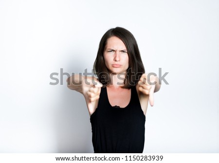 portrait of a young woman showing a thumbs down sign, dislike it, isolated studio photo on a gray background