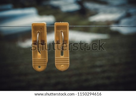 Couple plastic clothes peg. Royalty high quality stock photo of two yellow plastic clothes peg clothespin clipped on outdoor clothesline metal line. Green garden background