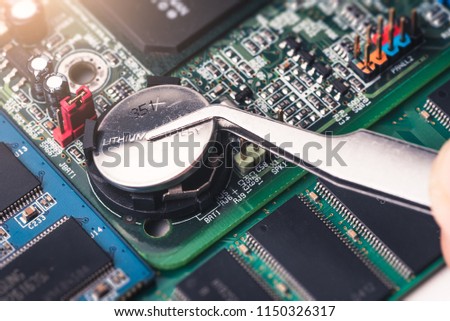 The technician is laying a cr2025 battery on the socket of the computer motherboard. the concept of computer, service, electronics, hardware, repairing, upgrade and technology. Royalty-Free Stock Photo #1150326317