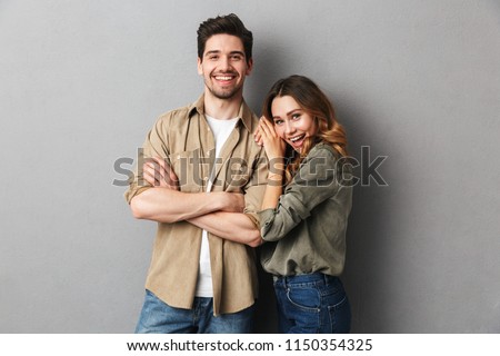 Portrait of a cheerful young couple standing together isolated over gray background, hugging Royalty-Free Stock Photo #1150354325