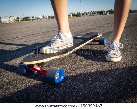Street high-speed sports: A girl in gray sneakers is rolling on a longboard along the road. Asphalt is smeared with speed.