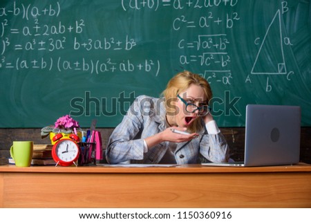 Work far beyond actual school day. Teacher busy with paperwork and research. Teacher tired face keep working after classes. Still working. Teacher woman sit table classroom chalkboard background.