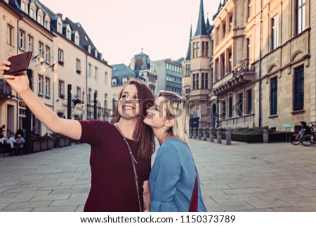 Two joyful cheerful girls taking a selfie while standing together outdoors, in the city center