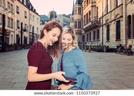 Two joyful cheerful girls taking a selfie while standing together outdoors, in the city center