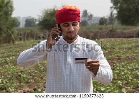 Farm worker holding credit card and talking on mobile phone in rural field Royalty-Free Stock Photo #1150377623