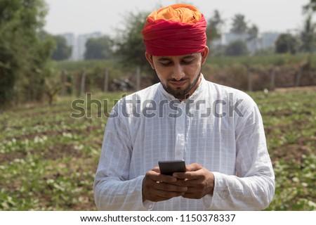 Farm worker text messaging on mobile phone in rural field Royalty-Free Stock Photo #1150378337