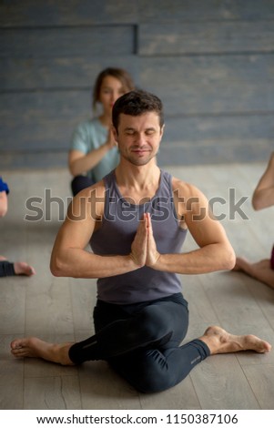 Young sportive male instructor practicing yoga with group of young women in studio over grey background. Training, Flexibility, Well-being Concept