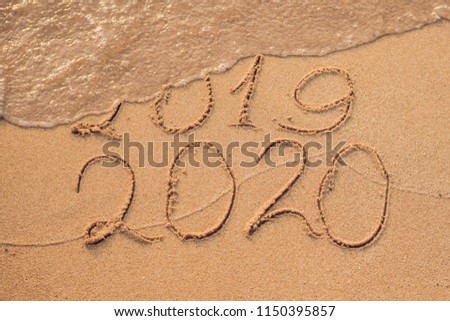 New Year 2020 is coming concept - inscription 2019 and 2020 a beach sand, the wave is almost covering the digits 2019 Royalty-Free Stock Photo #1150395857