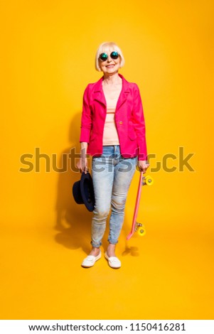 Full-body full-legh vertical portrait of modern elderly woman with a board for skating isolated on brigth yellow background