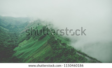 Aerial top view of sky road over top of mountain with fog and green jungle after raining in morning, Pua, Nan, Thailand. The transportation road across mountain. Shot from drone.