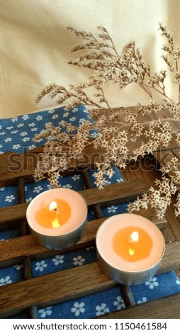 Two small burning candles on the wood and material with dry decorative flowers. Post greeting card background for holidays in vintage, rustic romantic style. Vertical photo