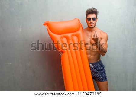 Young athletic man wearing a swimsuit against a grunge wall sad and depressed, making a gesture of need, restoring to charity, concept of poverty and misery