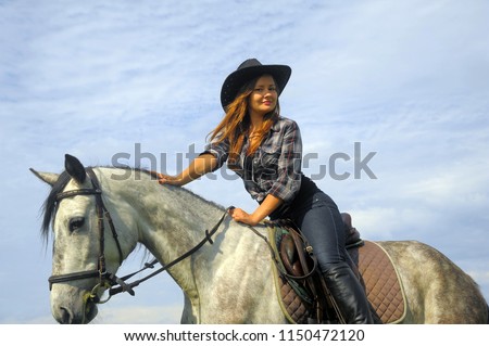 girl in plaid shirt and cowboy hat riding a horse by the lake
