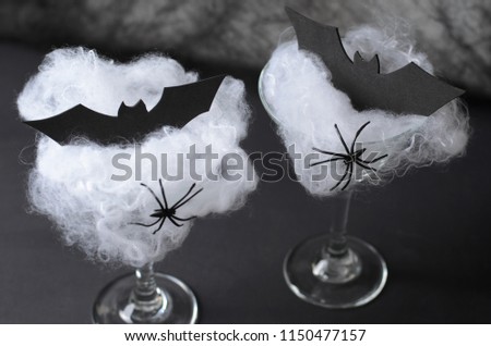 Halloween Cocktail Food Concept, Glass with Cobweb with Black Bat and Spider on Dark Background, Spooky Drink