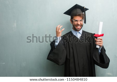 Young graduated man against a grunge wall with a copy space very angry and upset, very tense, screaming furious, negative and crazy