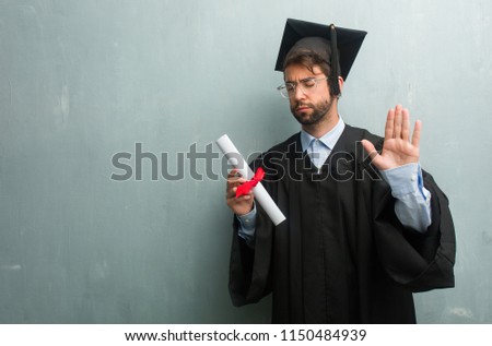 Young graduated man against a grunge wall with a copy space serious and determined, putting hand in front, stop gesture, deny concept