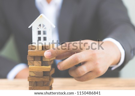 Businessman hand holding wood block with model white house. Investment risk and uncertainty in the real estate housing market. Property investment and house mortgage financial concept. with copy space