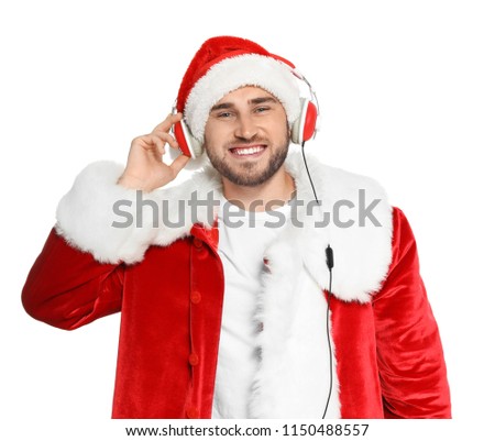 Young man in Santa costume listening to Christmas music on white background