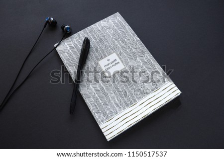 Image is Top view.Open note Paper and pen color gray with White earphone and black food background.