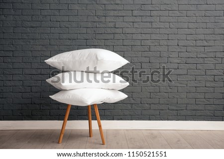 Pile of soft bed pillows on chair near brick wall with space for text Royalty-Free Stock Photo #1150521551