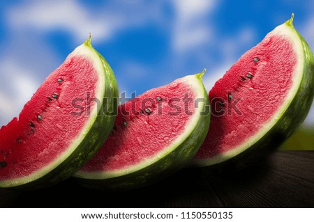 It's time for refreshment. Three pieces of very juicy and tasty watermelon on the wooden table up close. Nice blue skies and a background cloud. 