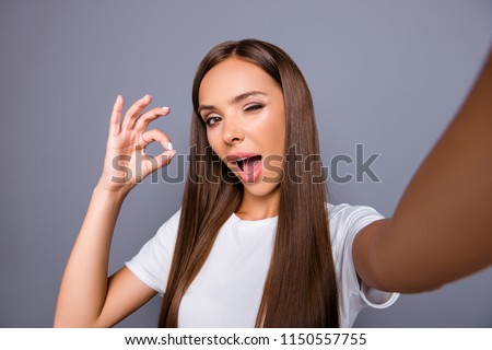 Close up picture of attractive brunette woman wink with open mouth shooting selfie, gesturing ok sign with fingers, having video call, standing isolated on gray background