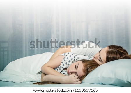Beautiful mom and lovely daughter are sleeping in white bed at home. Mother Day Concept.