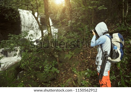 traveler photographing with backpack and enjoying a beautiful waterfall nature forest. 