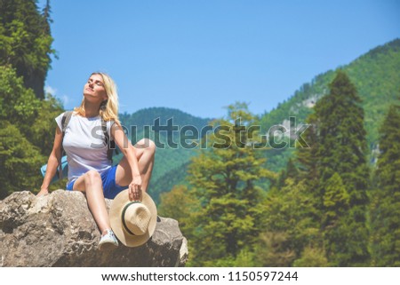 Beautiful Girl Traveler sits on a mountain and enjoys the sun on a background of mountains