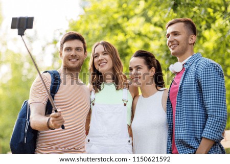 technology, travel, tourism and hike concept - group of smiling friends with backpack taking picture by smartphone and selfie stick in summer