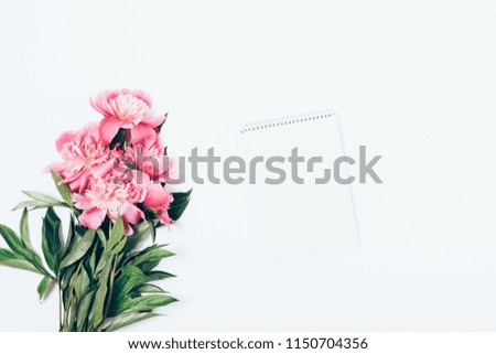 White feminine desktop mock-up with blank notepad sheet and pink peony flowers bouquet, top view. Flat lay concept of romantic diary, copy space.