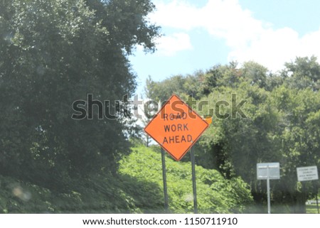 Orange road work sign surrounded by green forest.