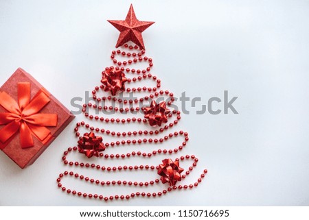 Creative idea in minimalistic style for Christmas or New Year themes. Christmas fir-tree from beads and a star on top. Nearby is a gift in a red box. Festive concept