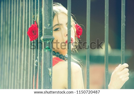 woman or spanish girl with fashionable makeup and red rose flower in hair, girl in black beads accessory on iron fence background, beauty and fashion