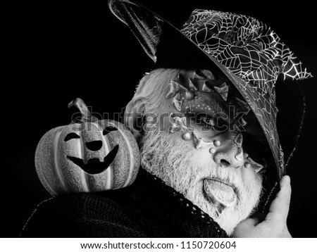 Sorcerer with dragon skin and grey beard on face. Wizard in witch hat on black background. Jack o lantern with spooky smile. Man with orange pumpkin. Magic and halloween concept.