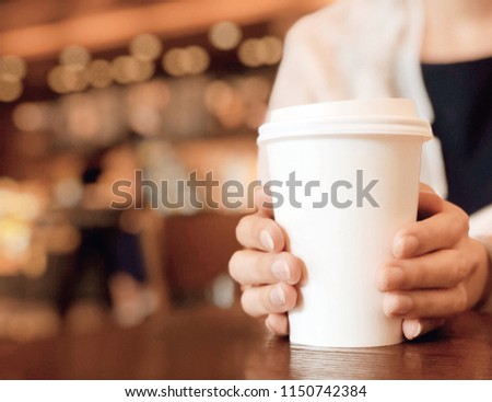 Hands in a warm gloves, holding coffee cup in coffee shop with copy space burry bokeh background.