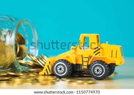 Mini bulldozer truck loading stack coin with pile of gold coin to glass jar, business finance and banking industrial concept idea.