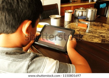 child with the tablet on table at tea time and breakfast