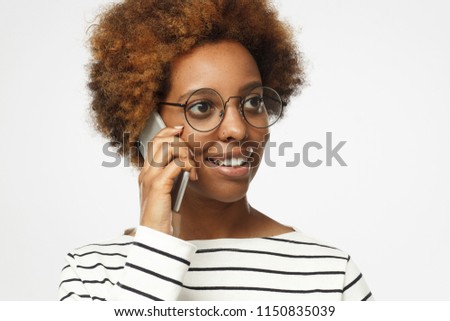Horizontal closeup of young African female pictured isolated on grey background wearing eyeglasses and dressed in striped top talking on phone for business needs feeling confident and positive