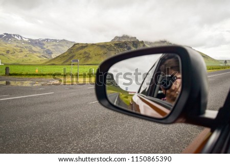 Man taking photo in rearview mirror of the view behind him.  Road trip concept.