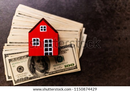 Red wooden house model over pile of money isolated on table background. Home money concept and free copy space.