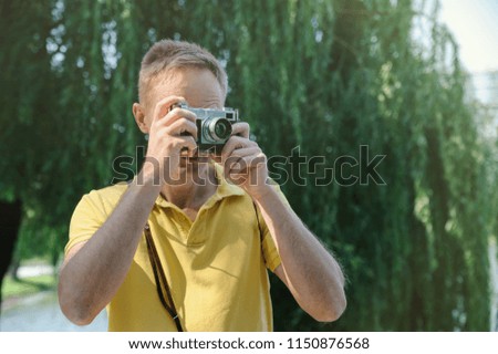 The man is photographing an old camera on a tree and lake background.