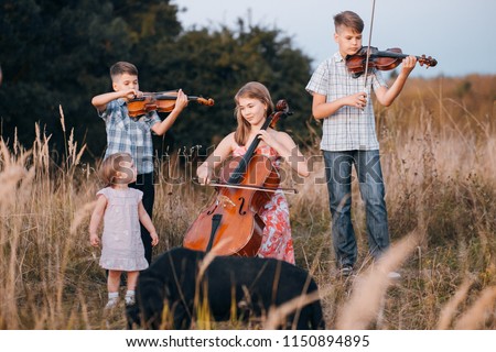 Children play on the violin and cello in a summer sunny field