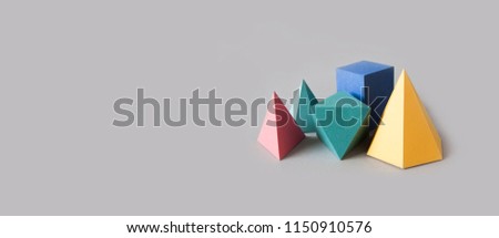 Colorful platonic solids, abstract geometric figures on gray background. Pyramid prism rectangular cube yellow blue pink green colored shapes. Shallow depth of field, copy space