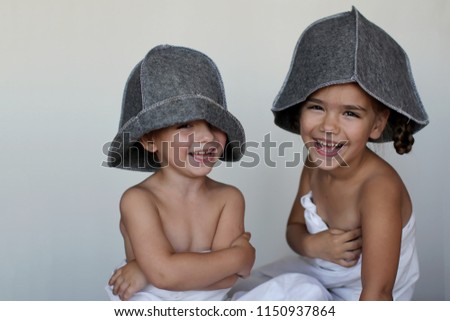 Funny little boy and girl, brother and sister, with bath hats on their heads and turned into white sheets smiling and looking at camera over white background, beauty and health concept, portrait