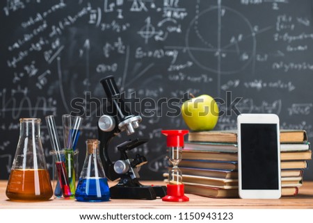 Tubes with chemical liquids stand on a wooden table on a chalkboard background with digital formulas